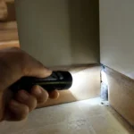 Dłoń z latarką sprawdza ciemną szczelinę za listwą w kuchni